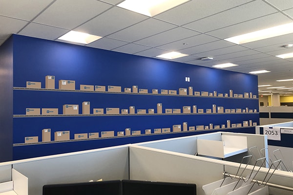 A blue wall with a vinyl graphic of conveyor belts with boxes on them